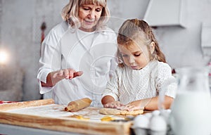 Senior grandmother with her little granddaughter cooks sweets for Christmas on the kitchen