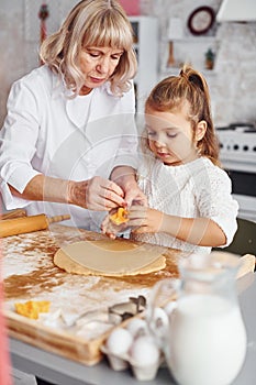 Senior grandmother with her little granddaughter cooks sweets for Christmas on the kitchen