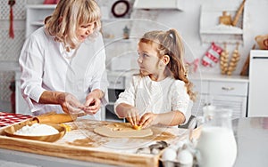 Senior grandmother with her little granddaughter cooks sweets for Christmas on the kitchen