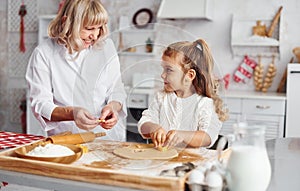 Senior grandmother with her little granddaughter cooks sweets for Christmas on the kitchen