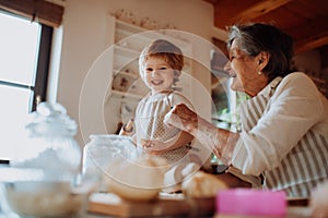 Senior grandmother with small toddler boy making cakes at home.