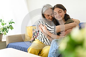Senior grandmother with teenage granddaguhter having good time together at home, hugging.