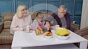 Senior grandparents and child granddaughter spending time home together, sitting, playing chess game