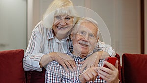Senior grandparents couple talking and using digital mobile phone at home. Coronavirus lockdown