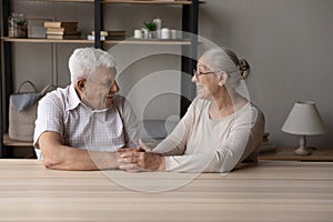 Senior grandparents sit at table holding hands feeling love