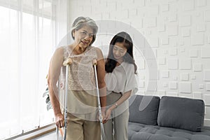 Senior gray hair woman exercise and practice walking at home. Young asian woman help her grandma walk by using axilla crutches photo