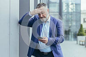 Senior gray-haired businessman in despair upset reading bad news on phone