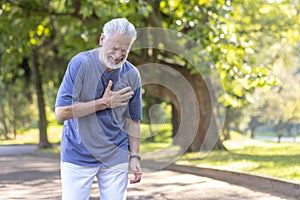 Senior gray-haired man suffering from a heart attack after walking and playing sports, standing in the park and holding