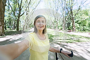 Senior gray-haired woman, active sportswoman with yellow bike in the park in the summer looks at the phone camera and smiles