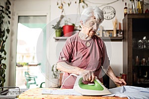 Senior gray-haired woman ironing laundry at home