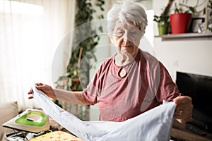 Senior gray-haired woman ironing laundry at home