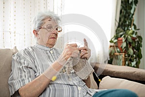 Senior gray-haired woman sitting on a sofa and knitting