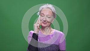 Senior gray haired woman in violet sweater talks on cellphone isolated on green chromakey background.