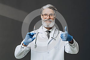 Senior grey hair doctor holding a syringe and looking at camera