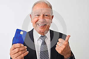 Senior grey-haired businessman holding credit card over isolated white background pointing and showing with thumb up to the side