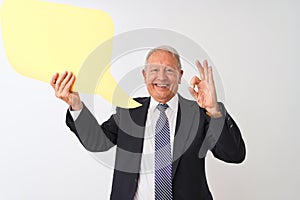 Senior grey-haired businessman holding speech bubble over isolated white background doing ok sign with fingers, excellent symbol