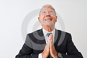 Senior grey-haired businessman wearing suit standing over isolated white background begging and praying with hands together with
