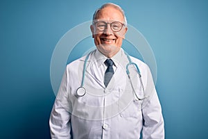 Senior grey haired doctor man wearing stethoscope and medical coat over blue background with a happy and cool smile on face