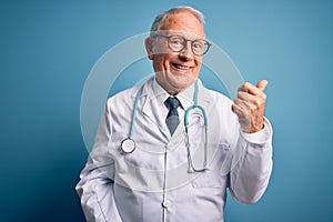 Senior grey haired doctor man wearing stethoscope and medical coat over blue background smiling with happy face looking and