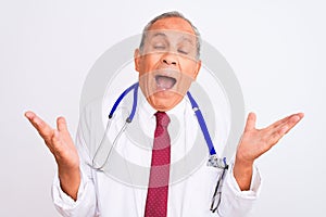 Senior grey-haired doctor man wearing stethoscope standing over isolated white background celebrating mad and crazy for success