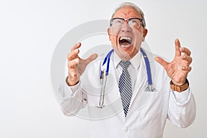 Senior grey-haired doctor man wearing stethoscope standing over isolated white background crazy and mad shouting and yelling with