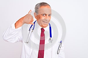 Senior grey-haired doctor man wearing stethoscope standing over isolated white background smiling doing phone gesture with hand