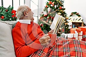 Senior grey-haired man drinking coffee and reading book celebrating christmas at home