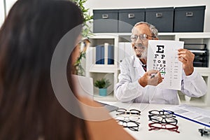 Senior grey-haired man optician doing snellen eye test to patient at clinic