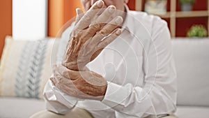 Senior grey-haired man sitting on sofa suffering for wrist pain at home