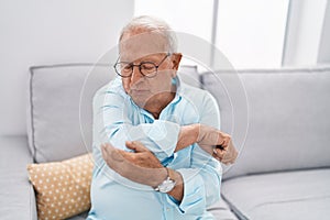 Senior grey-haired man suffering for elbow pain sitting on sofa at home