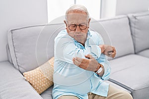 Senior grey-haired man suffering for elbow pain sitting on sofa at home