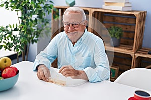 Senior grey-haired man taking pills sitting on table at home