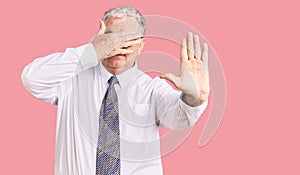 Senior grey-haired man wearing business clothes covering eyes with hands and doing stop gesture with sad and fear expression