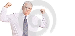 Senior grey-haired man wearing business clothes showing arms muscles smiling proud