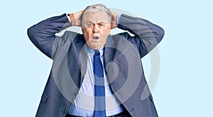 Senior grey-haired man wearing business jacket crazy and scared with hands on head, afraid and surprised of shock with open mouth