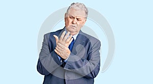 Senior grey-haired man wearing business jacket suffering pain on hands and fingers, arthritis inflammation