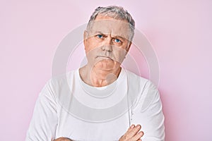 Senior grey-haired man wearing casual white tshirt skeptic and nervous, disapproving expression on face with crossed arms