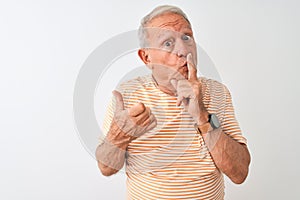 Senior grey-haired man wearing striped t-shirt standing over isolated white background asking to be quiet with finger on lips