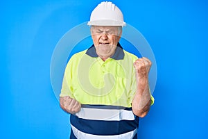 Senior grey-haired man wearing worker reflective t shirt and hardhat celebrating surprised and amazed for success with arms raised