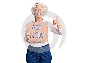 Senior grey-haired woman holding act now banner smiling happy and positive, thumb up doing excellent and approval sign