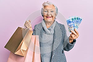 Senior grey-haired woman holding shopping bags and south africa rands banknotes smiling with a happy and cool smile on face