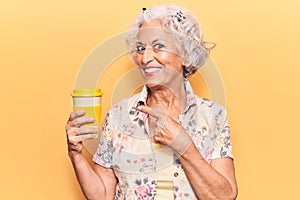 Senior grey-haired woman holding takeaway cup of coffee smiling happy pointing with hand and finger