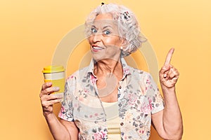 Senior grey-haired woman holding takeaway cup of coffee smiling happy pointing with hand and finger to the side