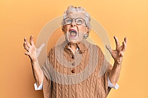 Senior grey-haired woman wearing casual clothes and glasses crazy and mad shouting and yelling with aggressive expression and arms
