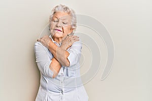 Senior grey-haired woman wearing casual clothes hugging oneself happy and positive, smiling confident