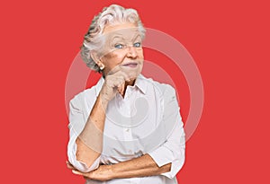 Senior grey-haired woman wearing casual clothes looking confident at the camera with smile with crossed arms and hand raised on