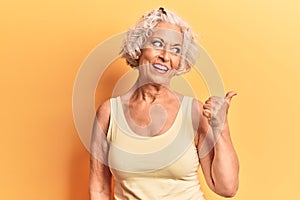 Senior grey-haired woman wearing casual clothes smiling with happy face looking and pointing to the side with thumb up