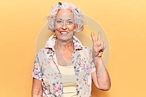 Senior grey-haired woman wearing casual clothes smiling with happy face winking at the camera doing victory sign