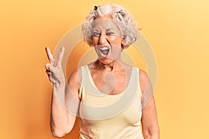 Senior grey-haired woman wearing casual clothes smiling with happy face winking at the camera doing victory sign with fingers