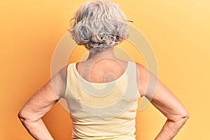 Senior grey-haired woman wearing casual clothes standing backwards looking away with arms on body